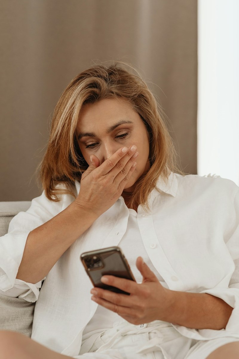 Woman looking at her phone, shocked, with her hand covering her mouth