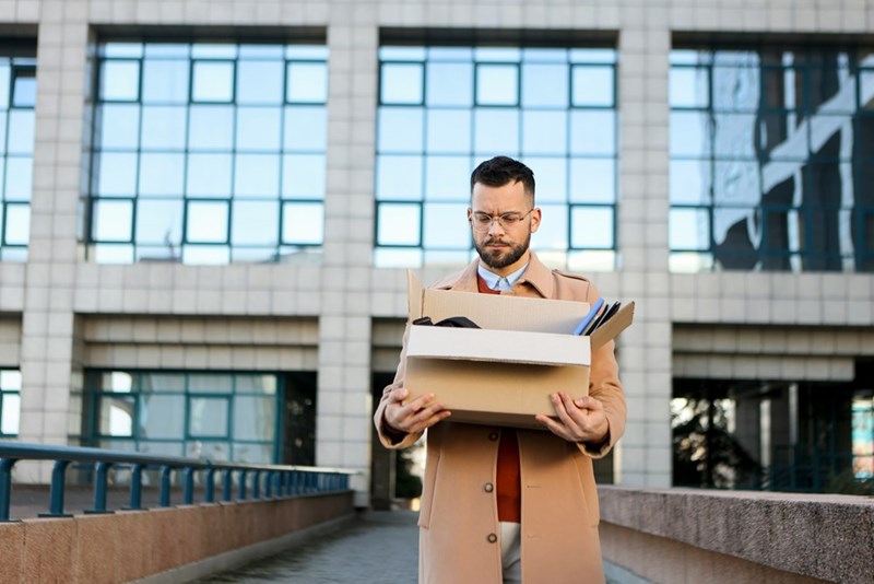 An employee walks out the front doors of the office building with a box of their belongings
