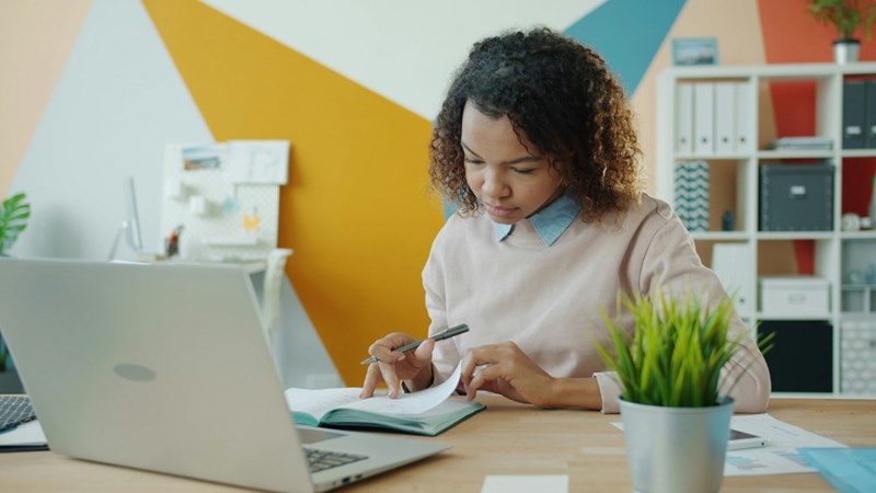 Woman working at a desk with a laptop and notebook
