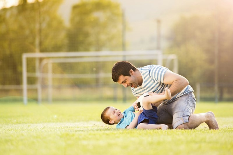 Young father with his little son playing football on football pitch