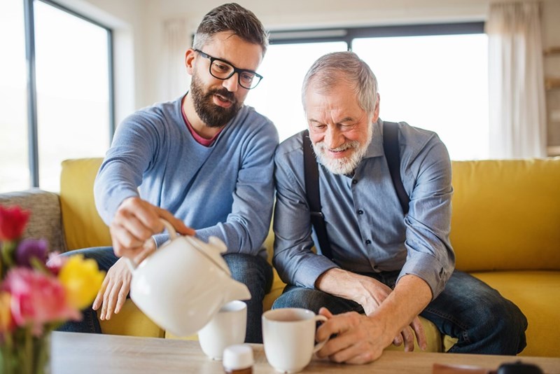 A father and son enjoy tea together, smiling as they spend quality time in a cozy living room.