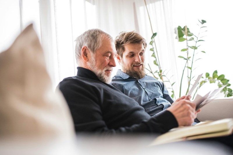 A father and son sit together on a couch, looking through papers and sharing a quiet moment.