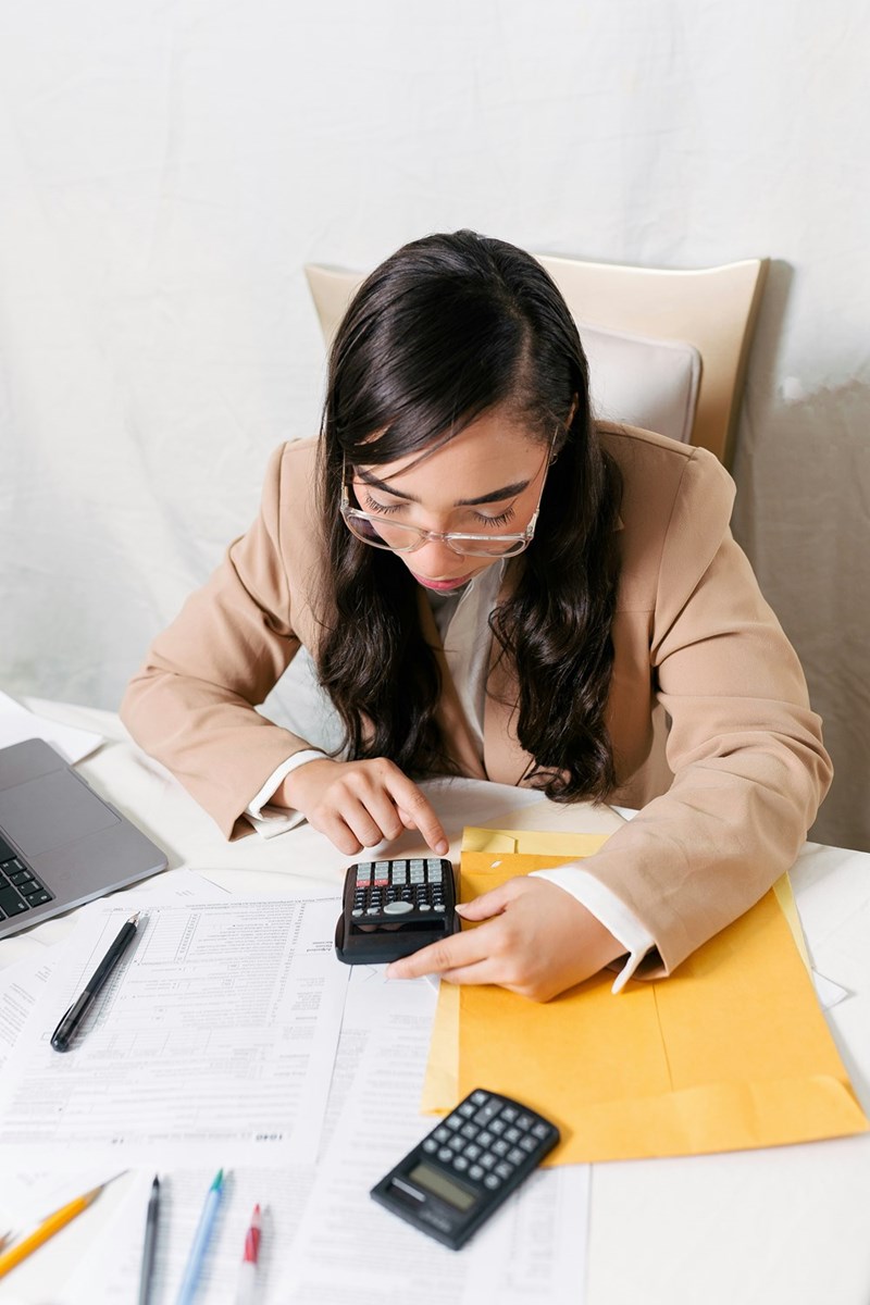 Woman sitting at a desk with a calculator and a laptop.