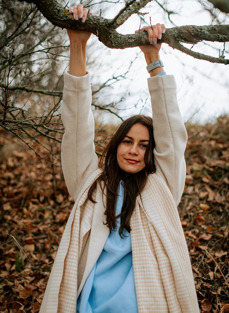 Woman hanging from a tree branch outdoors, surrounded by fallen leaves, looking relaxed.
