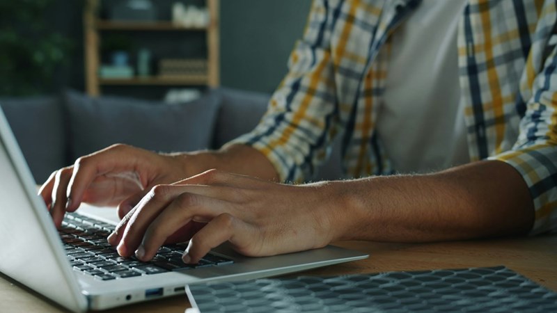 A man types on a laptop at home