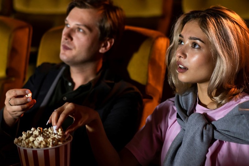 Teen girl and her friend watch a movie together in a theater.