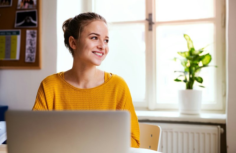 Teenager smiles while using computer, thinking about how she plans to get thousands of dollars from her friend.