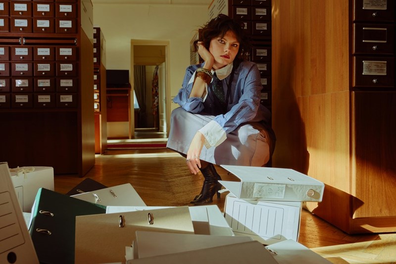 Office worker squats down to pick up numerous binders she dropped on the floor.