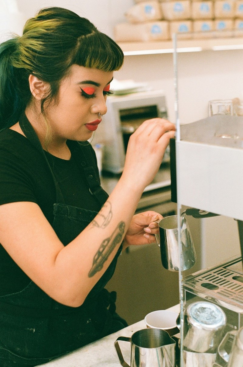 A woman with green hair making coffee at her barista job