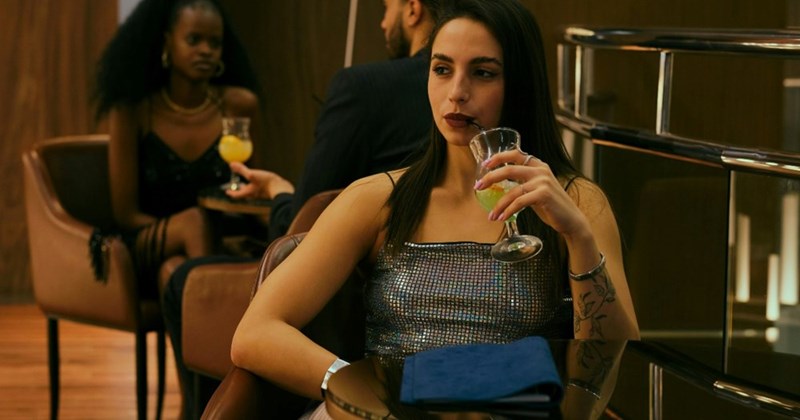 A woman sits at a table sipping a drink at a bar.