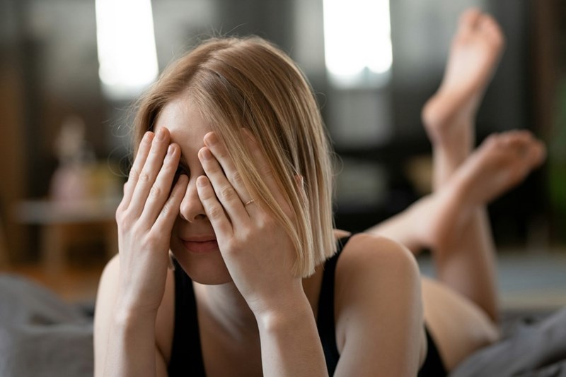 A young woman lies on her stomach, covering her face with her hands in a moment of quiet frustration.