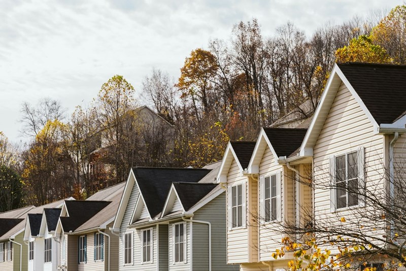 A row of similarly built suburban homes surrounded by autumn trees and a cloudy sky