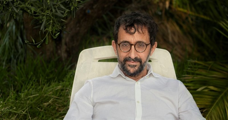 A homeowner in a white dress shirt sits in a white chair in his backyard.