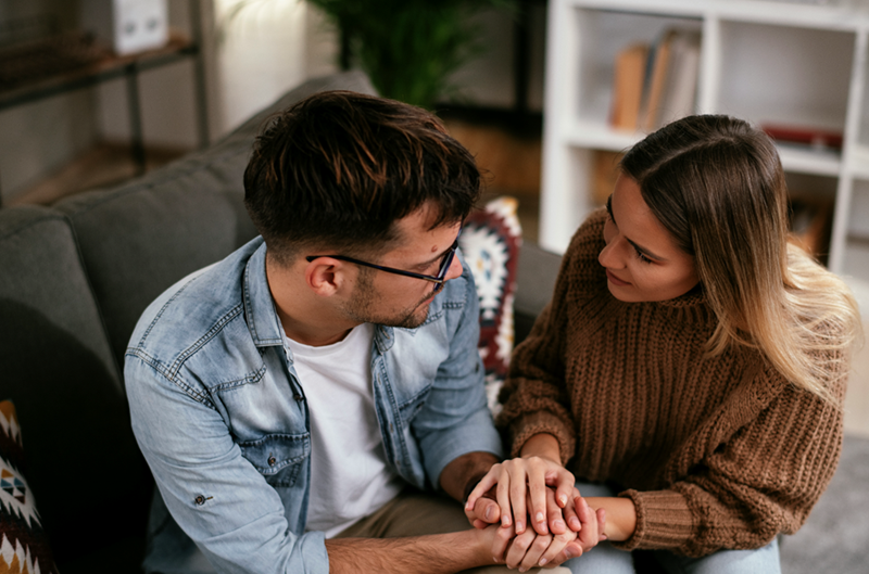 Overhead shot of a couple holding hands on the couch as they confront one another.