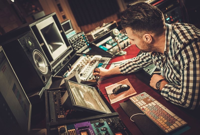Man working in a recording studio, adjusting audio equipment while focused on the mixing console and screens.