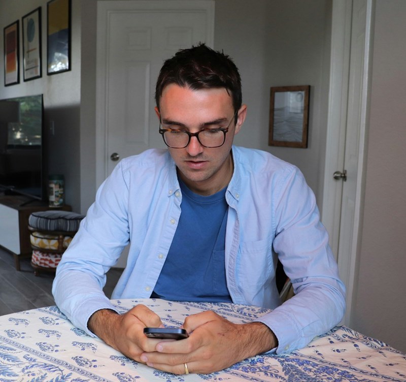 Man sitting at a table, looking down at his phone with a focused or slightly concerned expression.