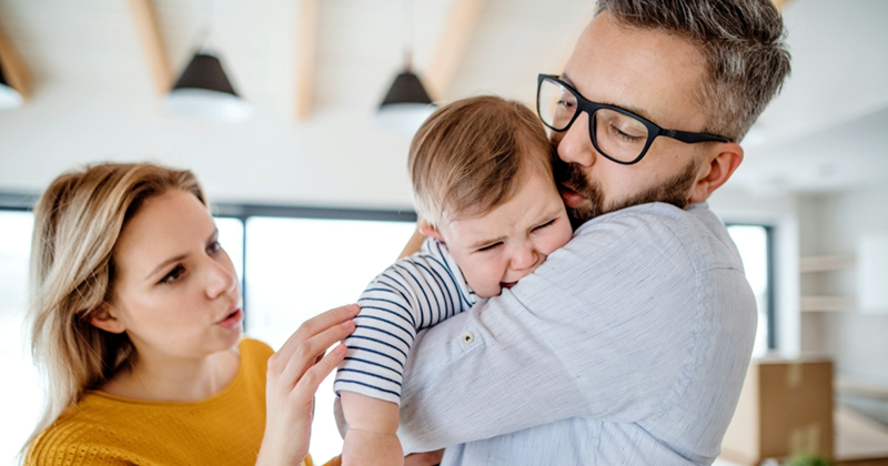 A young mom soothes a crying baby being held by her father
