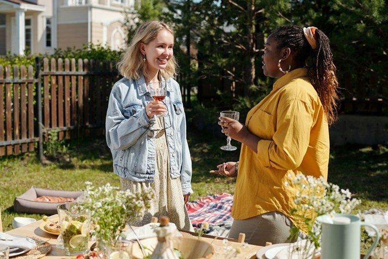 Young black woman and blonde Caucasian girl with glasses having a chat during outdoor party by the food table