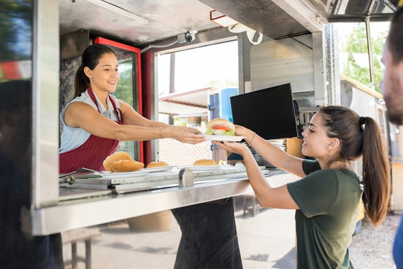 A food truck worker hands a hamburger to a customer
