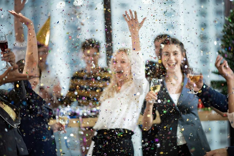 Coworkers celebrate during an office party as confetti falls.