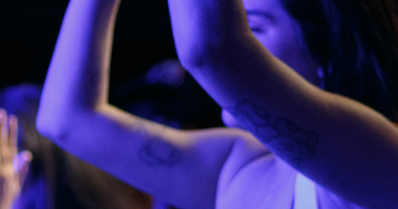 A woman raises her hands above her head in the crowd at a concert