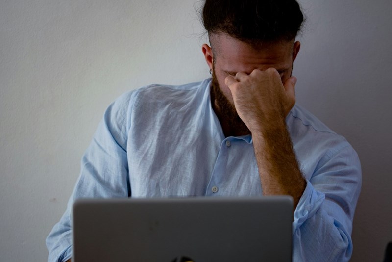 A man in a blue shirt looks frustrated at his desk