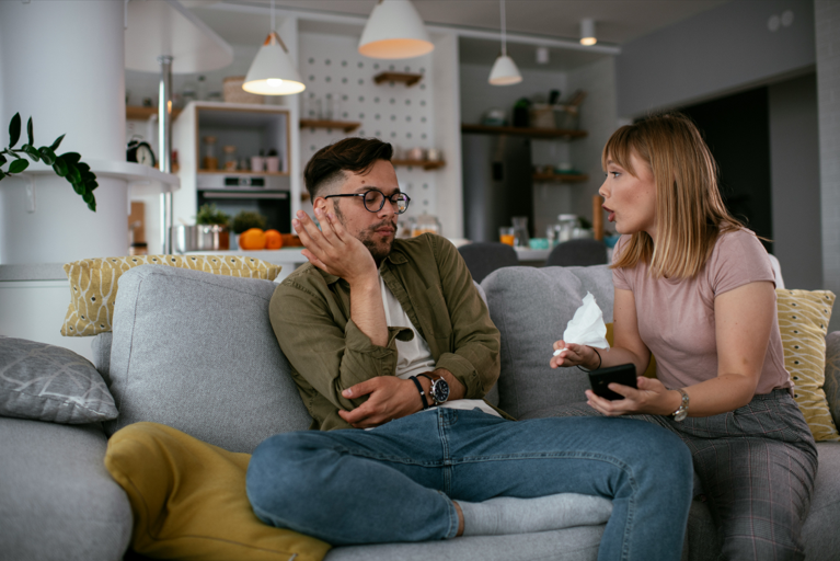Boyfriend and girlfriend sitting down on a couch discussing.