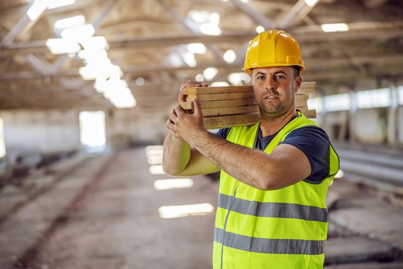 Picture of hardworking construction working holding joists while walking on construction site.