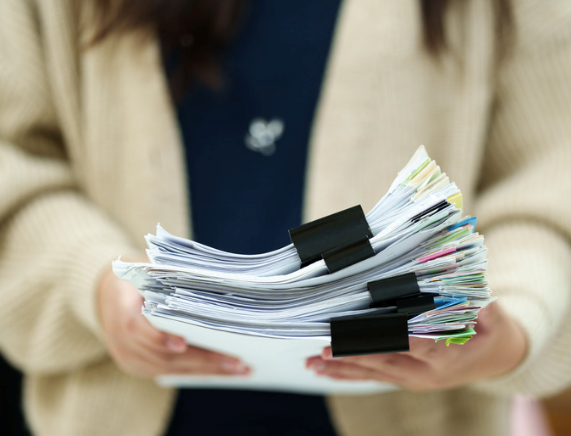 Woman carrying an enormous stack of paperwork to her boss's office.