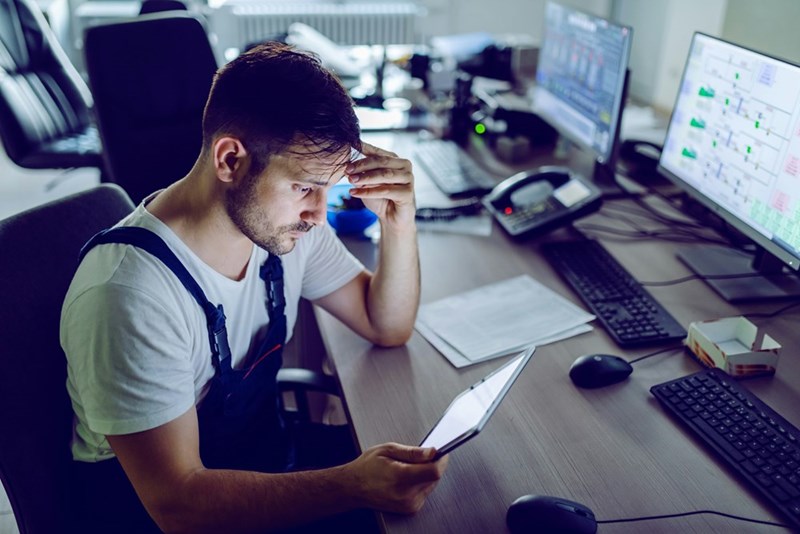 A man looks at a tablet at his desk, upset.