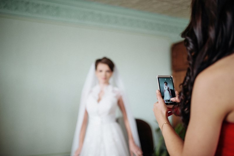 Friend taking pictures of bride in her wedding dress.