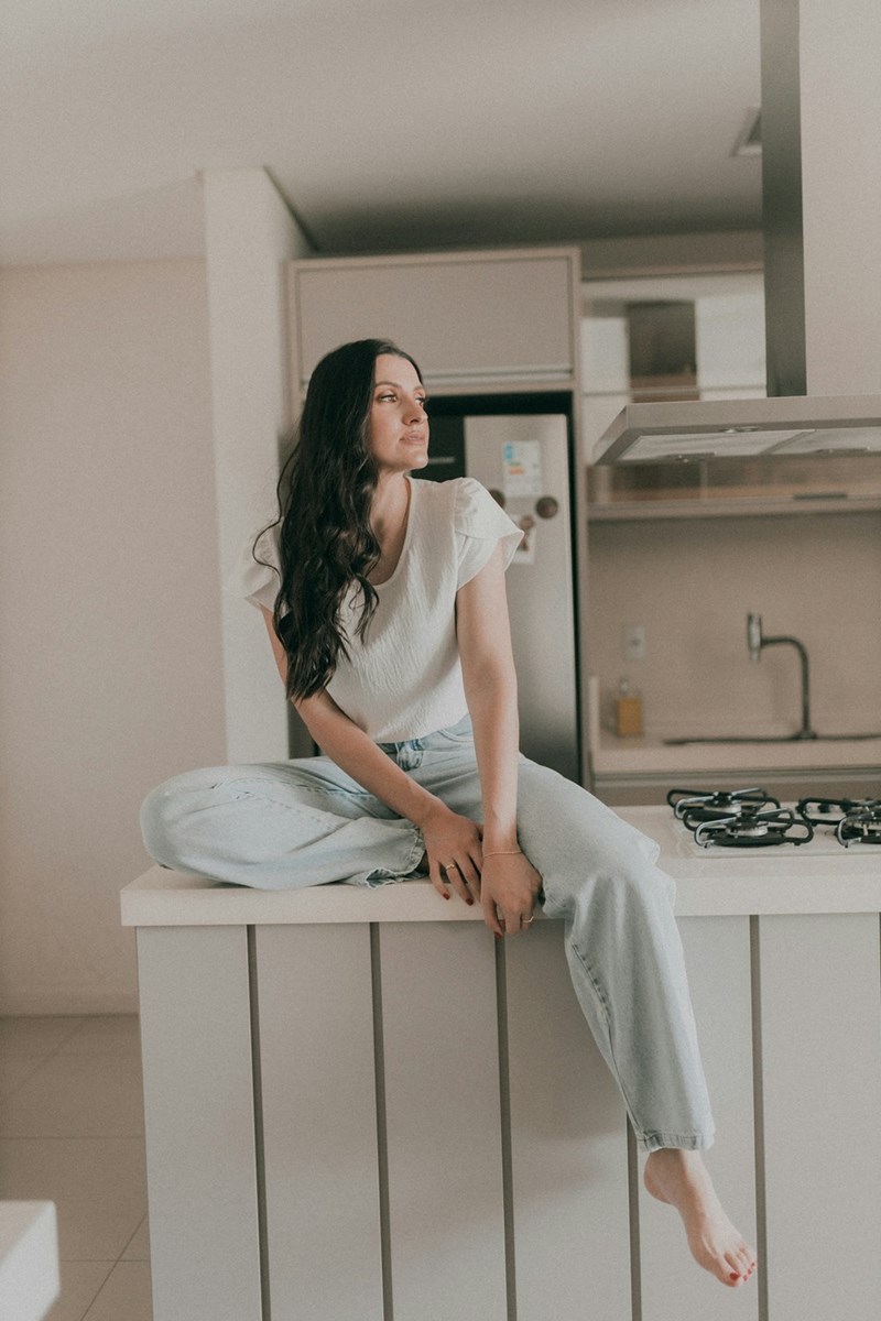 Woman sitting on a kitchen counter, looking off to the side with a calm, thoughtful expression.