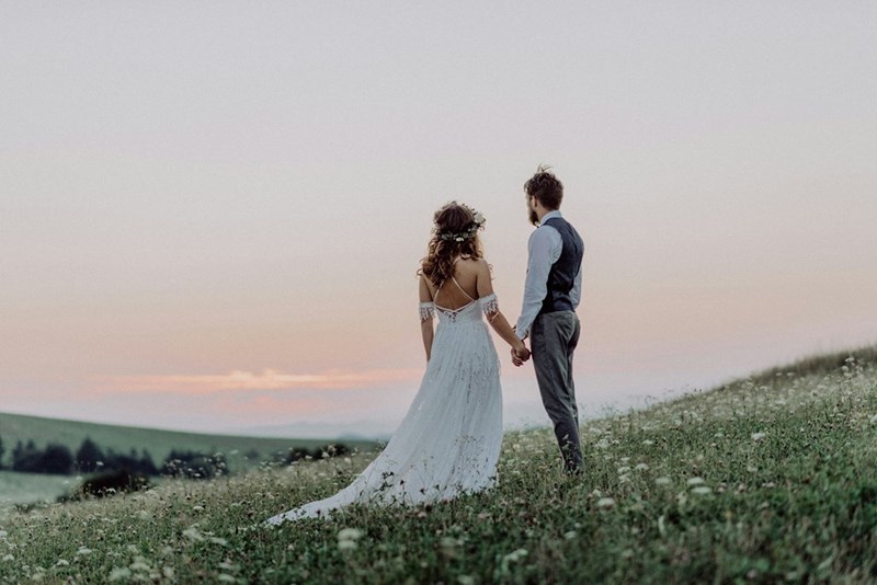 A beautiful bride and groom stand looking out at the vista toward the sunset.