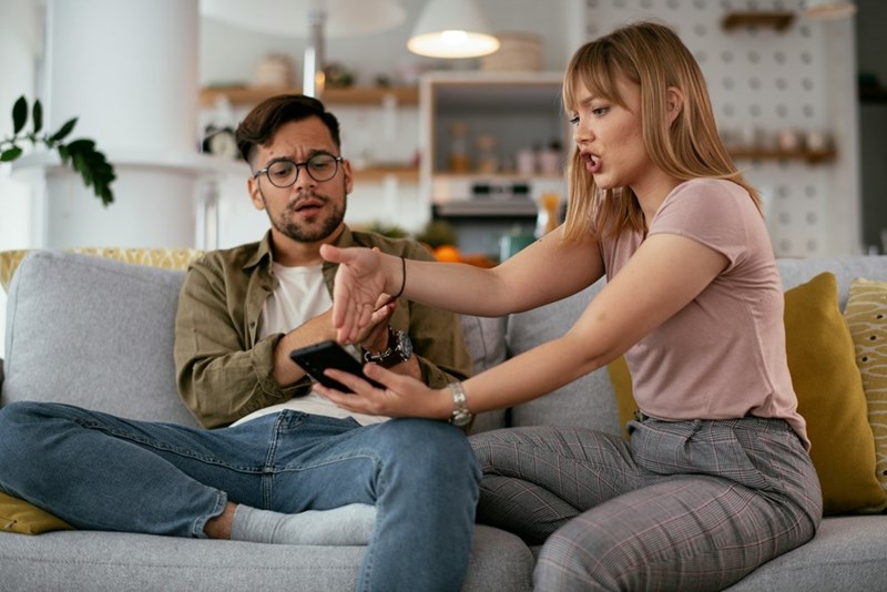 Couple arguing on couch about phone during relationship conflict at home