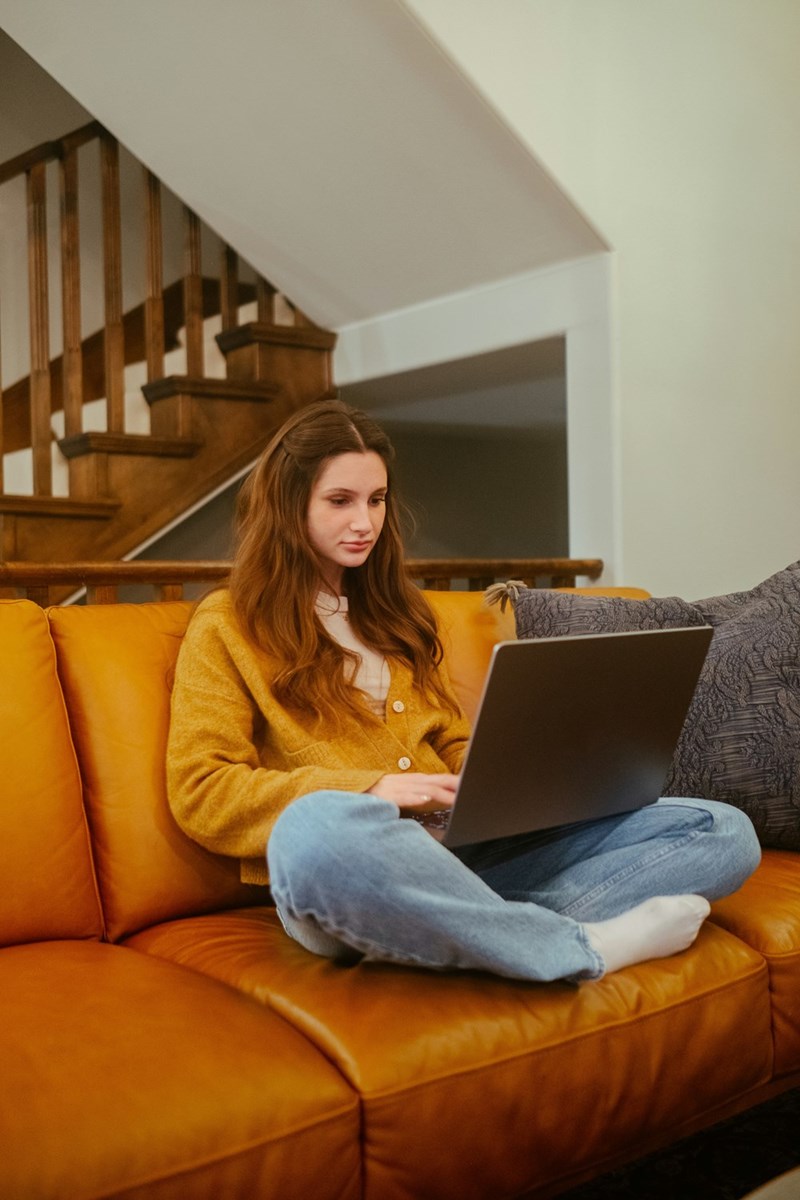 Group of one woman sitting cross-legged on a couch using a laptop in a cozy living room.