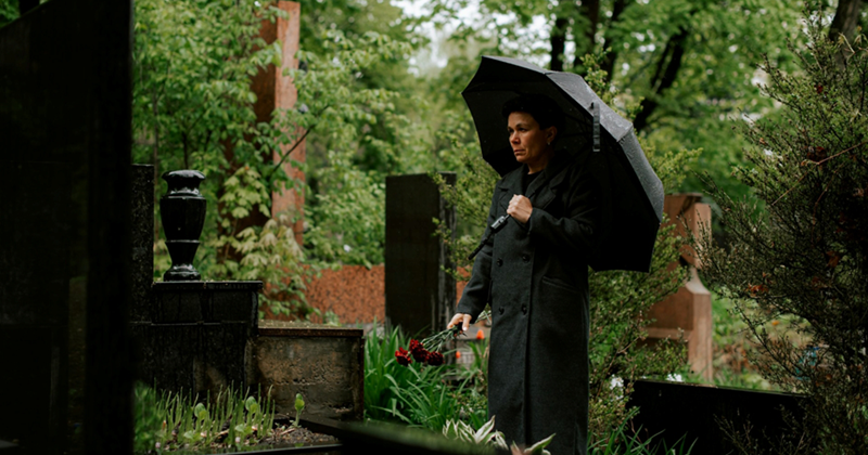 A woman holding an umbrella over her head stands in the middle of a cemetery