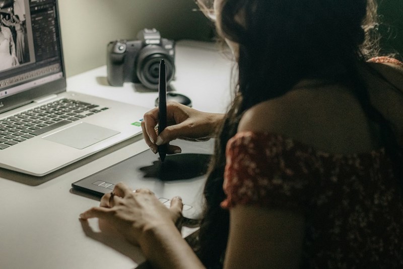 Woman sitting on her work desk designing something with a tech bar and a pencil.