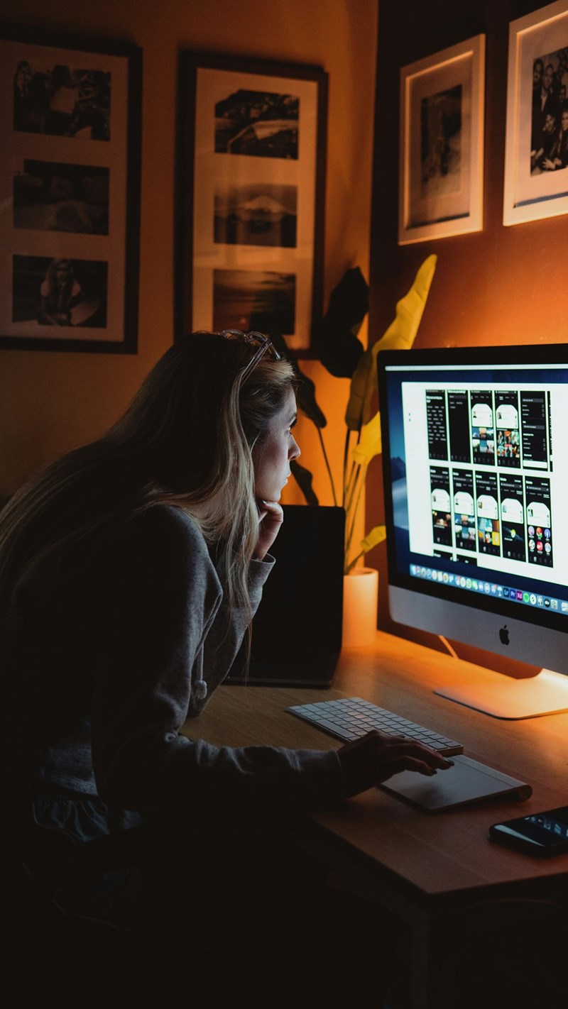 Woman is sitting in a desk at night while looking at a program in a computer.