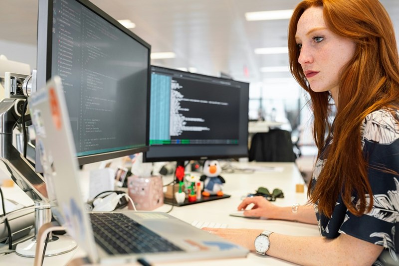 Software engineer works at her desk with a laptop and 2 computer monitors.