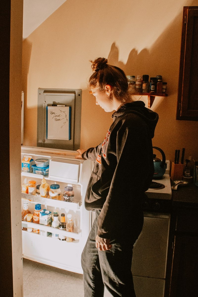 Woman in sweatshirts looking for food in the fridge at night.