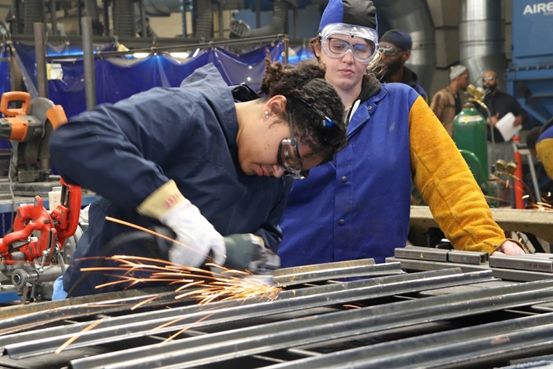Trade school student watches as a professional welder works