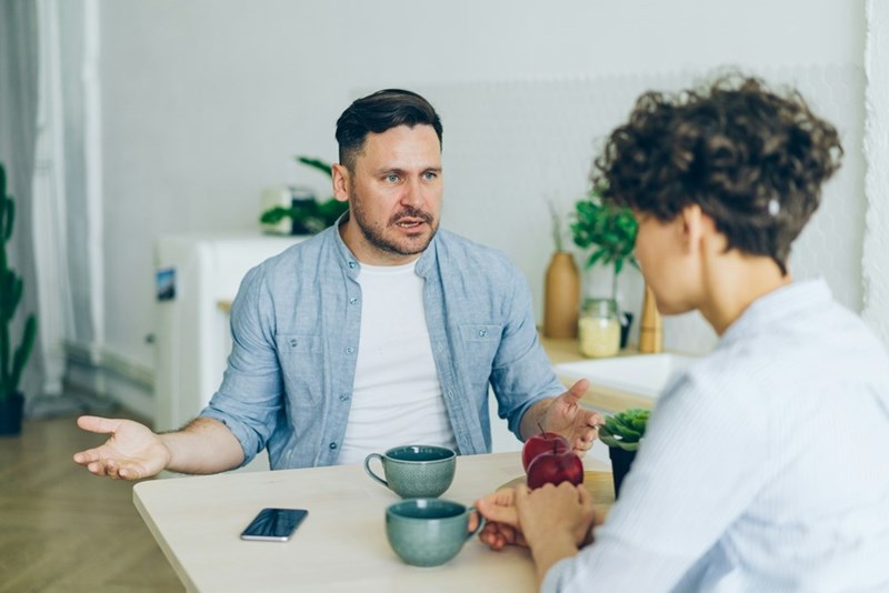 Man arguing at kitchen table during relationship conflict and emotional confrontation