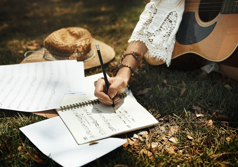 Woman writing song lyrics in notebook outdoors with acoustic guitar and autumn setting