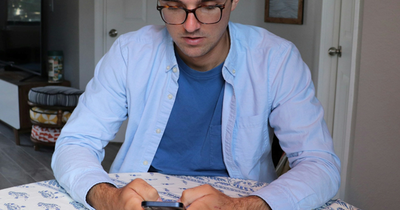 A man sits at a table at home, looking at his phone
