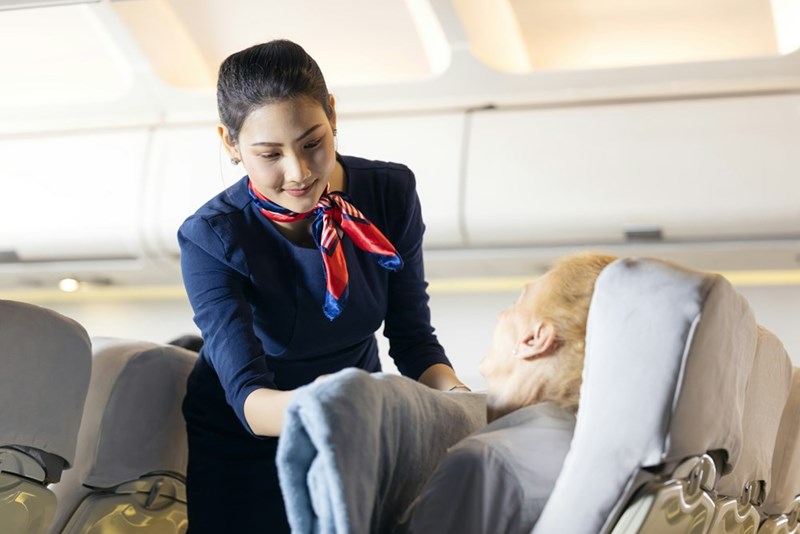 A female flight attendant helping an elderly passenger sleeping in the passenger seat