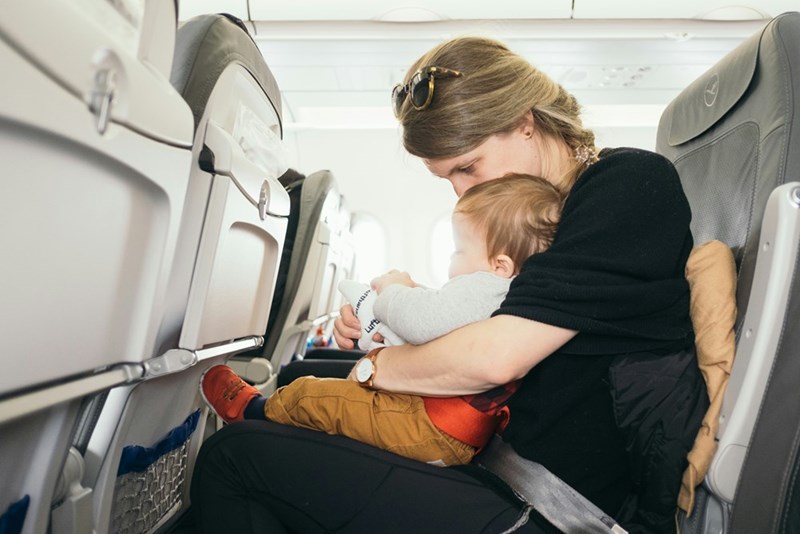Mom comforts her baby while they sit together on a plane.