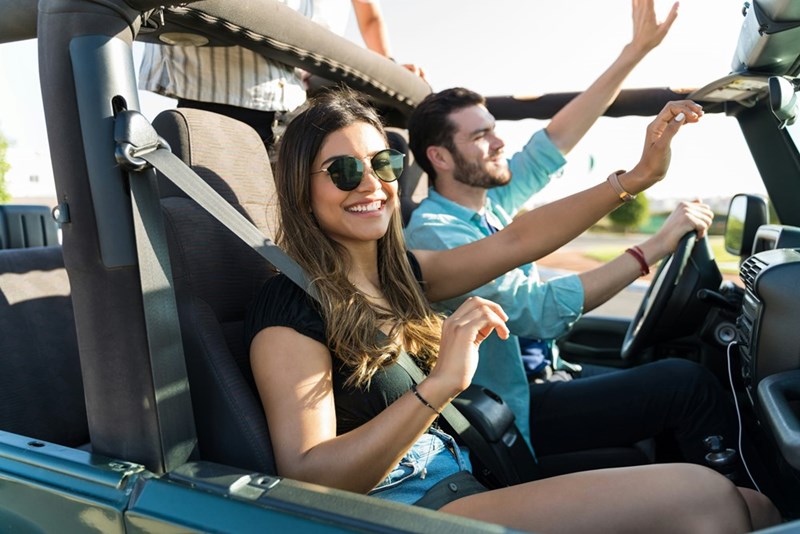 Smiling woman and man drive around in a convertible 4x4 car with their hands up. 