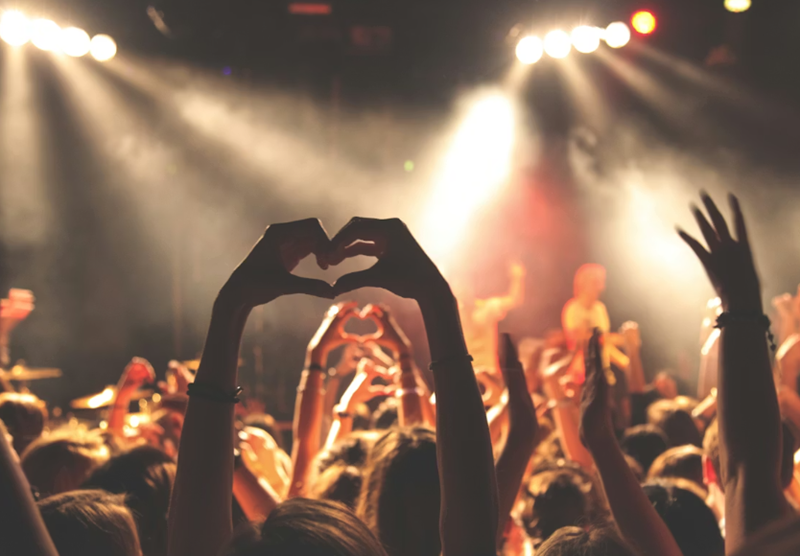 A crowd of people in a concert with their hands in the air.