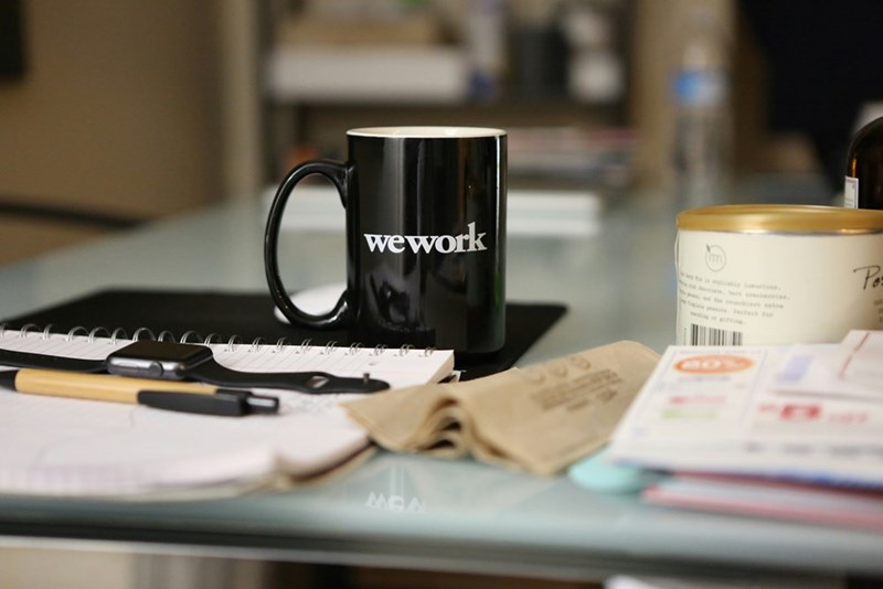 A black ceramic WeWork mug sits atop an empty desk.
