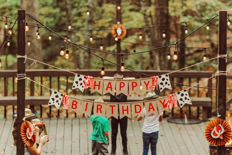 Rustic outdoor birthday party setup with decorations and string lights in a forest setting